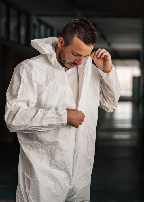 worker-taking-off-white-uniform-while-standing-hallway-school-after-disinfecting (1)